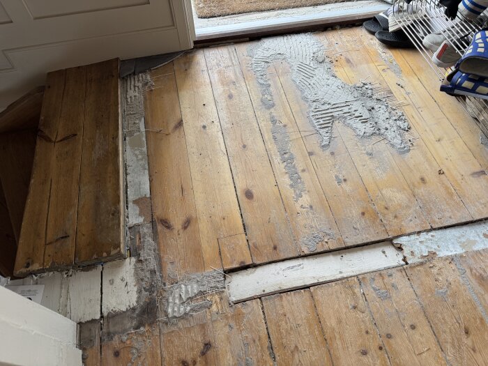 Slitet furugolv med rester av lim eller nät synliga och en skåra mellan plankorna, där arbete har påbörjats för att avlägsna materialet.
