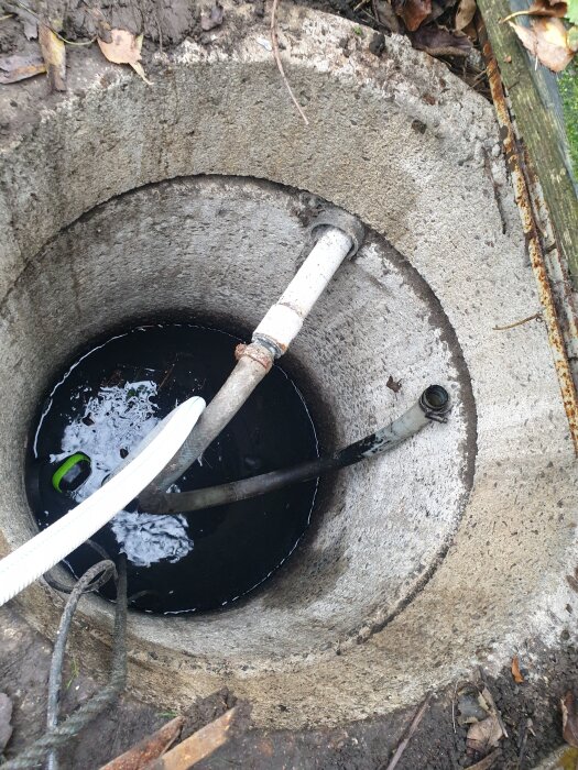 Betongbrunn med vatten och tre slangar, inklusive en vit, kopplade för att lösa ett stopp i vattenpumpningen mot fördelningsbrunn.