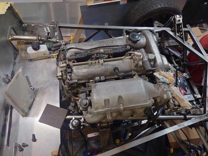 Motor av en Miata NB 1,8 liters radfyra monterad i en ram, med verktyg och bildelar utspridda runt arbetsområdet.