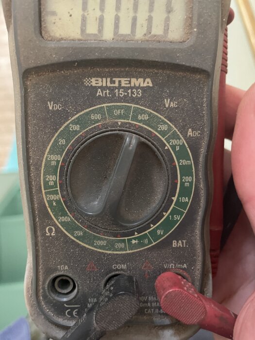 Multimeter med ratt och mätstickor för att kontrollera om kablar är strömlösa, används vid elarbete i ett rum.