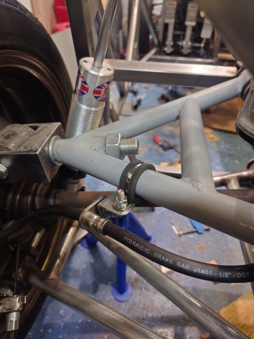 Ett grått vinkeljärn på en ram med monterad bromsledning och fjädring, del av ett fordonsprojekt i ett verkstadsgolv.