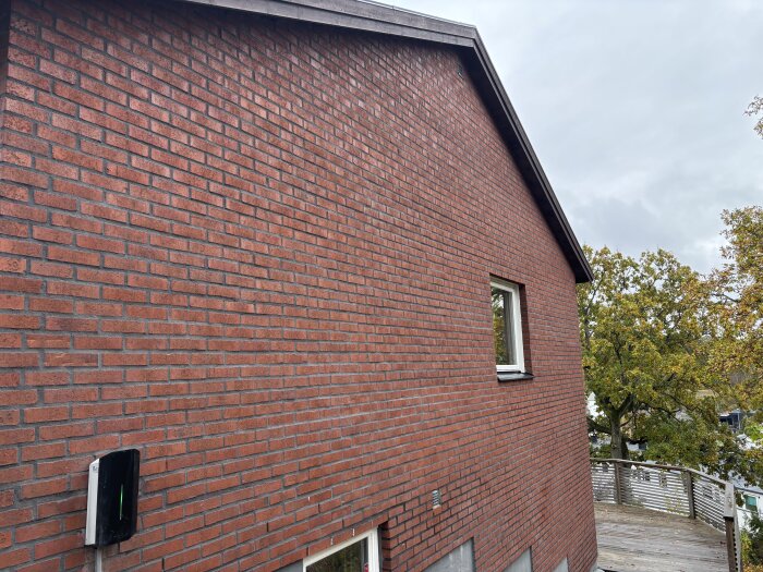 Fasad med tegelvägg och ett litet fönster, omgiven av höstträd. Ställningen är riven och fasaden är nyligen klar.