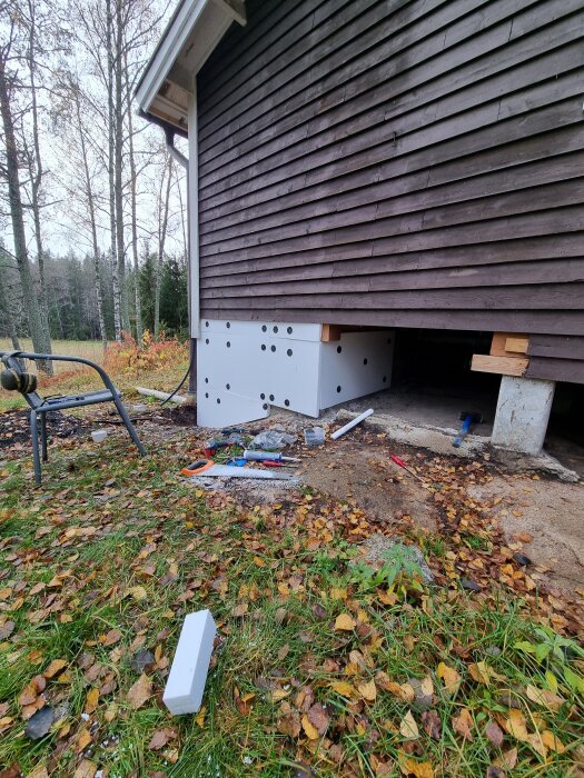 Lecablock och isolering med cellplast syns på ett husbygge, med verktyg och byggmaterial utspridda på marken framför.