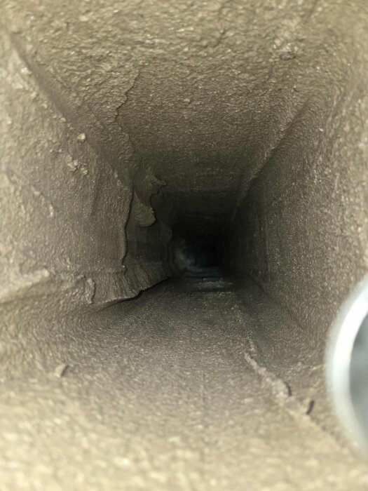 Inuti en murstock efter glidgjutning, sedd från sotluckan med en tydlig rektangulär öppning och ojämn yta.