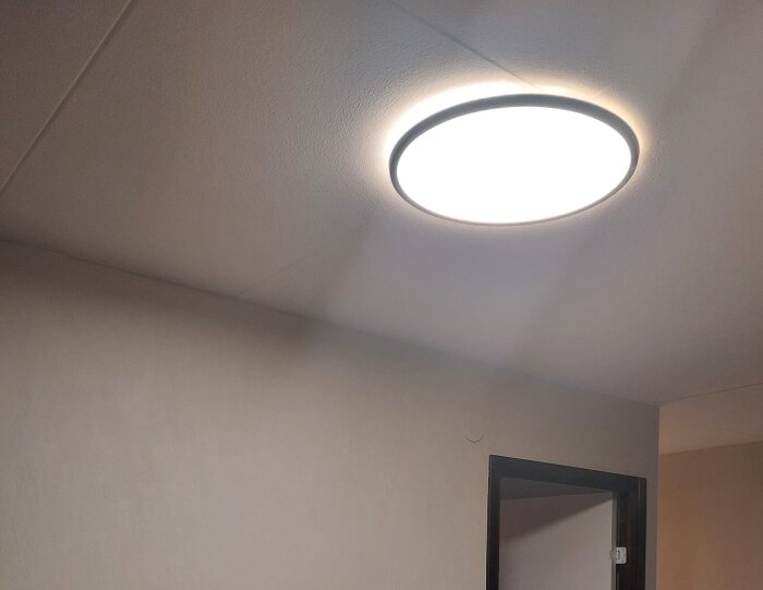 Taklampa monterad och tänd i ett rum med beige väggar.