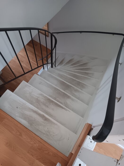 Vit trappa med svarta räcken i ett äldre radhus. Stegen är slitna inför ommålning.