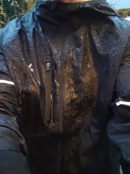 Person i en blöt regnjacka med reflexdetaljer, fotograferad utomhus i dåligt väder.