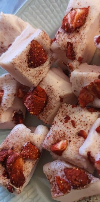 Kubformade marshmallows med torkade jordgubbar och kanel, liggande på en ljusgrön tallrik.