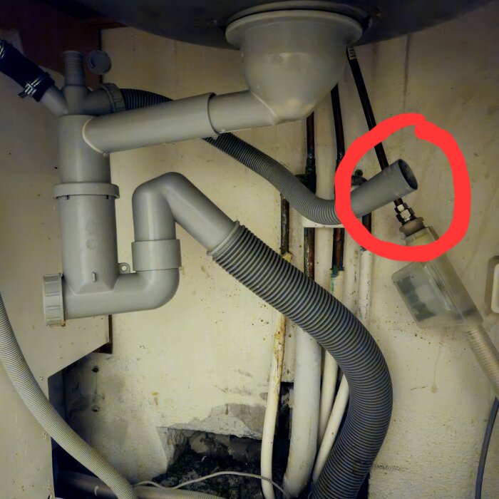 Under sink plumbing with multiple pipes, one highlighted in red, indicating a potential leak or blockage issue.