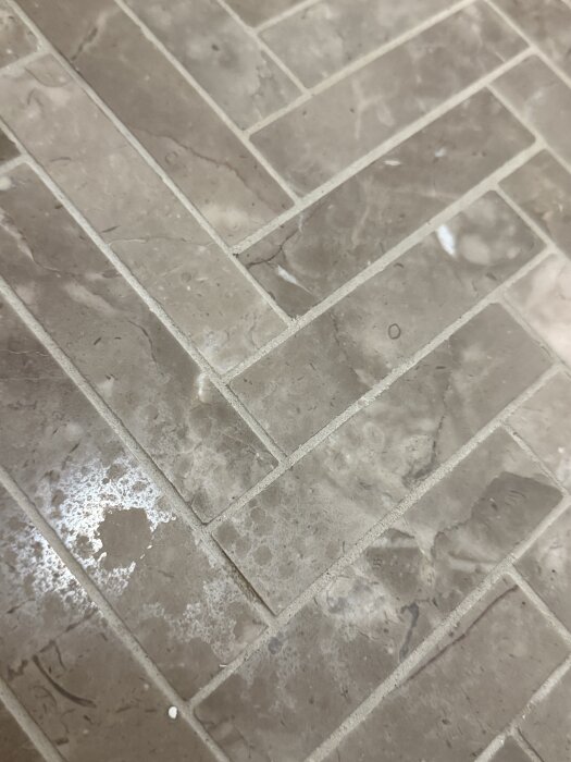 Golv av kalksten i badrum med synliga vita fläckar och märken efter användning av anti-kalkmedel.