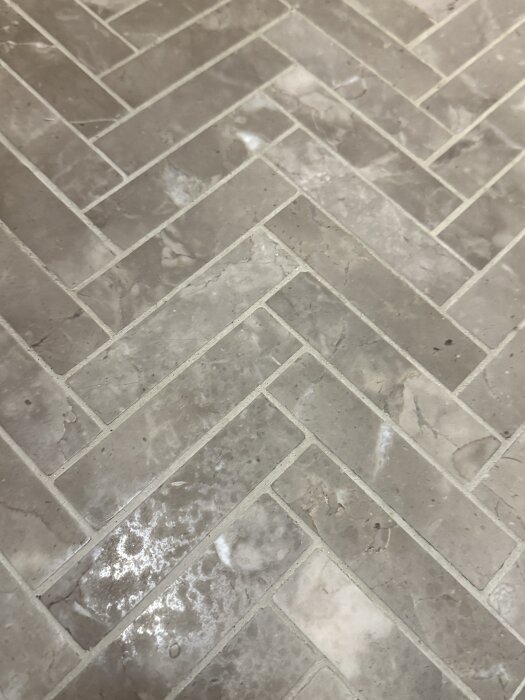 Golv av kalksten i fiskbensmönster med synliga ljusa märken efter rengöring med anti-kalkmedel.
