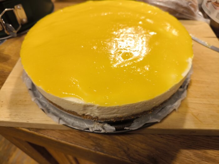Mango cheesecake med gul glasyr på en skärbräda, gjord med gelatin istället för bakad med ägg i traditionellt recept.