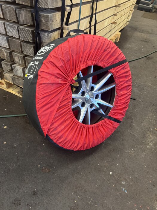 Inpackat sommardäck i röd och svart skyddspåse, placerat framför staplade träplankor.