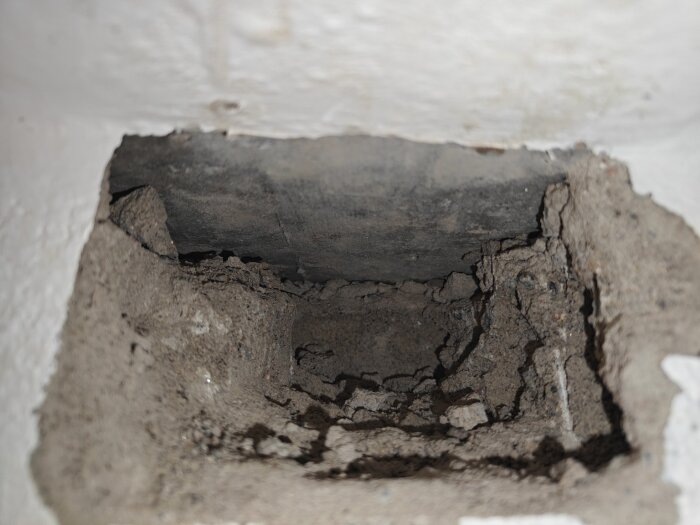 Närbild av ett vägguttag med exponerade tegelfragment och gjutningsspår, antyder tidigare borrhål i väggen som ska undersökas för bärighet.