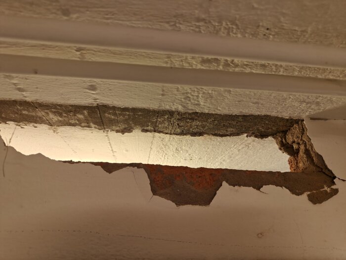 Närbild på en uppbruten del av en innervägg som visar synligt tegel och betong under ytskiktet.