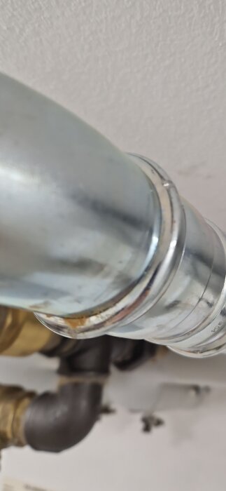 En elförzinkad presskoppling i 54mm diameter med ett runt utseende visas i närbild monterad på ett rörsystem.