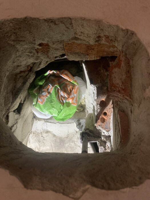 Öppning i skorsten för installation av eldstadskassett, visar murade kanter och en grön plastpåse i hålet.