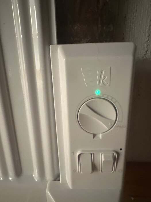 En vit elektrisk elementregulator med en på/av-knapp och en grön indikatorlampa synlig.