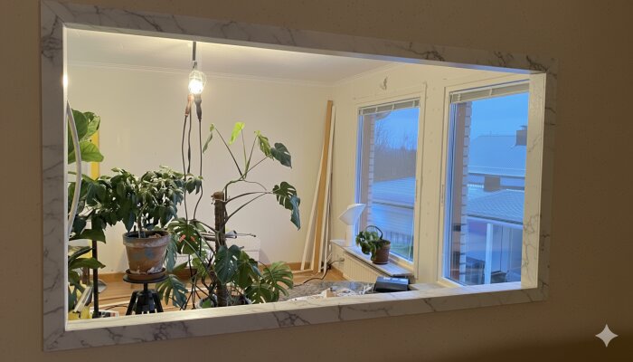 Fönster med en marmorliknande fönsterkarm, inomhusväxter i förgrunden och utsikt mot ett snötäckt tak utanför.
