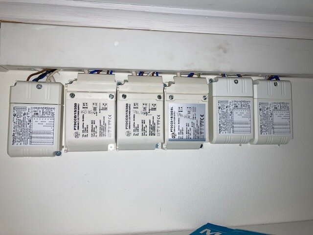 Sex elektriska drivdon monterade på en vit vägg, med flera kablar anslutna vid toppen, i en garderob.