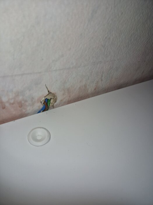Kablar som sticker ut ur väggen ovanför en vit badrumshylla, lösa och synliga utan täckning.
