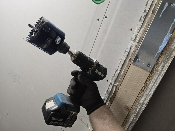 En person använder en Makita-borrmaskin med en hålsåg för att göra ett märke i gipsväggen, förbereder för arbetet efter gipsning.