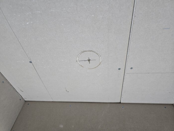 Gipsvägg med cirkulärt märke från hålsåg, omgiven av skruvar. Förberedelse för elinstallation i renoveringsprojekt.