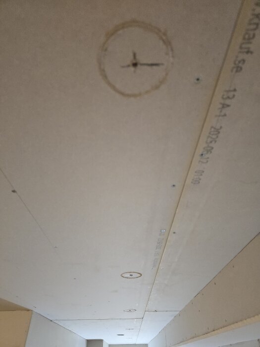 Närbild på gipsvägg med hålmarkeringar för borrning. En stor cirkel med skåror indikerar plats för framtida installationer.