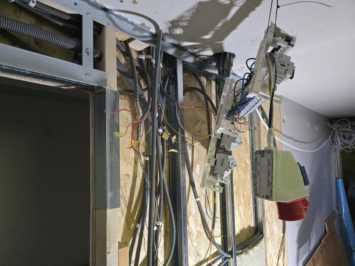 Elektriska ledningar och kopplingsdosor hänger från en vägg under renovering, omgivna av exponerade kablar och byggmaterial.