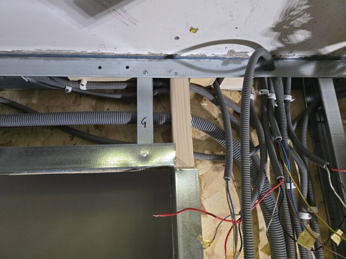 Elledningar och kabelrör i takstruktur, med trä- och metallstöd. Kablarna går genom gråa flexrör, och några är märkta med gula etiketter.