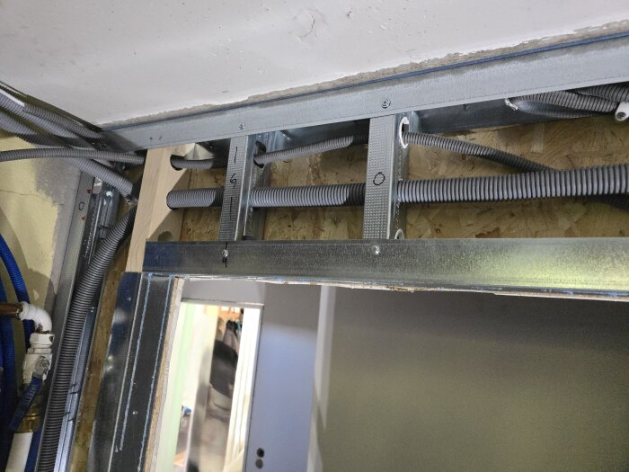 Byggnadsvägg med synliga elkablar och flexrör i en öppning, del av renoveringsprojekt i en korridor eller tvättstuga.