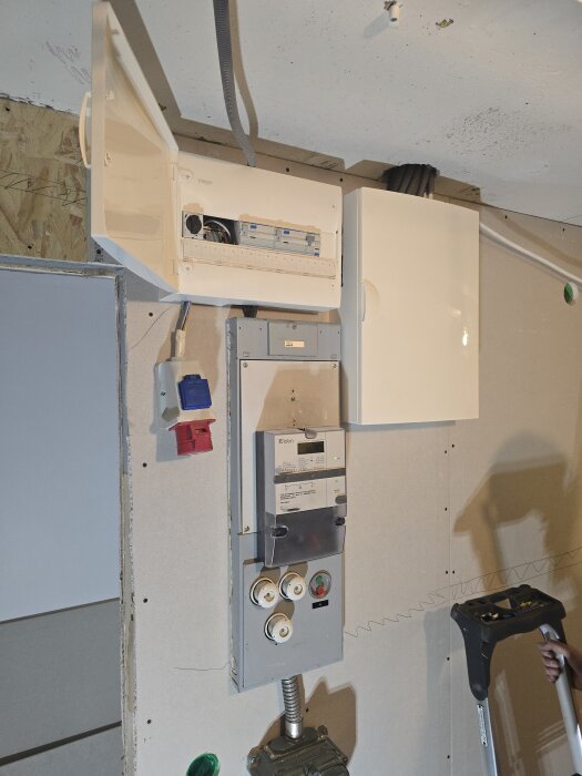 Elcentral med flera kopplingsdosor och kablar monterad på en ny gipsvägg. En oskyddad kabel och en stege syns också.