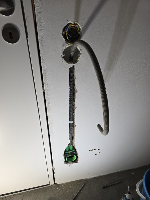 Elektrisk installation i vägg med synliga ledningar och kabelrör, bredvid dörrkarm. Hål för eluttag förberett med monteringsdosa.