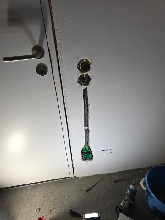 Vägg med två dosor och elinstallation vid dörrkarm, slangar och verktyg på golvet bredvid.