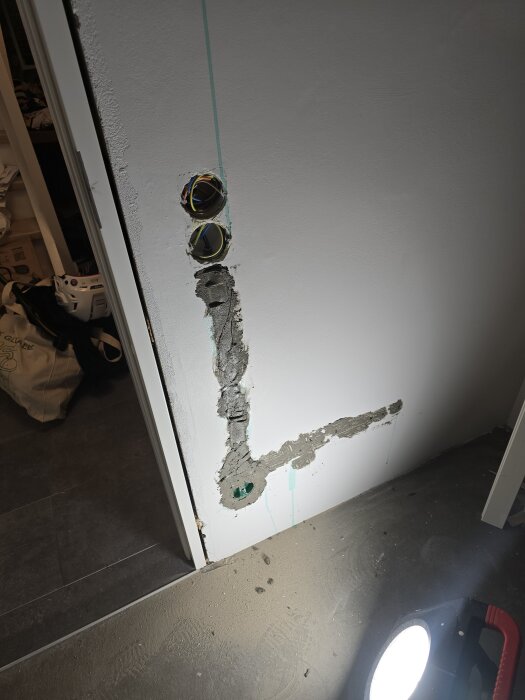 Vägg med två infällda eldosor och spår urtaget för eldragning i gips. Golv med verktyg och damm syns i förgrunden.