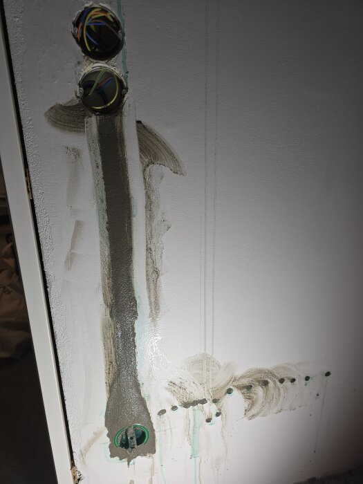 Elinstallation i vägg med öppna dosor och kabeldragning, hål och spackelarbete synligt på väggen, redo för fortsatt bearbetning.