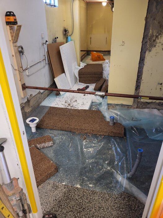 Renovering av källare med cellplast, isodrän och makadam på golvet, verktyg och byggmaterial synliga i rummet.