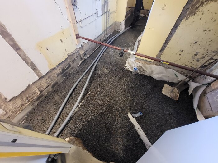 Renovering av källare med synlig makadam på golvet och inslag av byggmaterial och verktyg. Väggar visar murbruk och rörarbete.