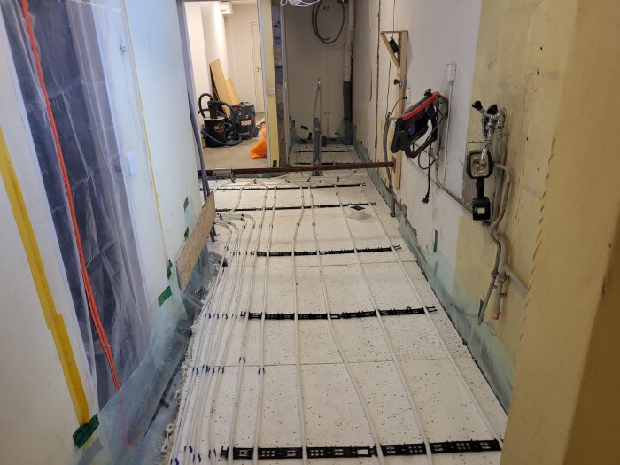 Renovering av källare; golvvärmerör installerade på vit cellplast, verktyg och material syns i bakgrunden av arbetsutrymmet.