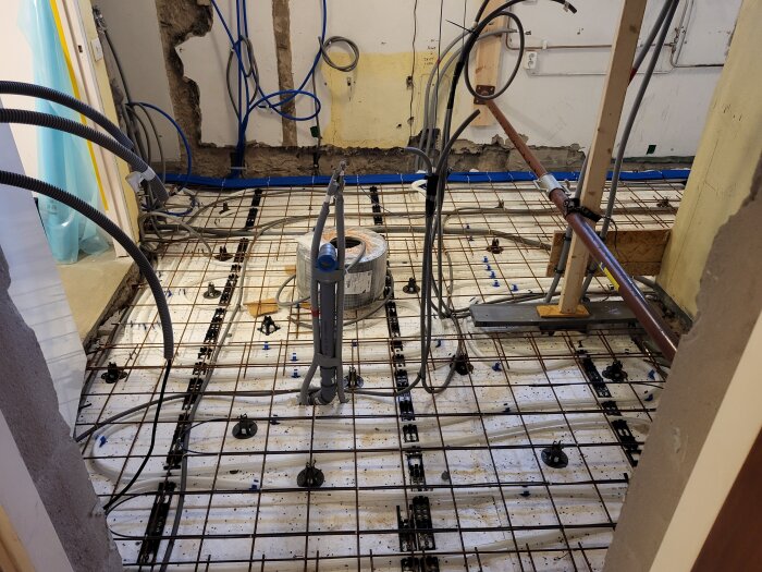 Renoveringsprojekt i källare med synliga armeringsjärn, kablar och rördragningar på ett betonggolv med isodrän och makadam som underlag.