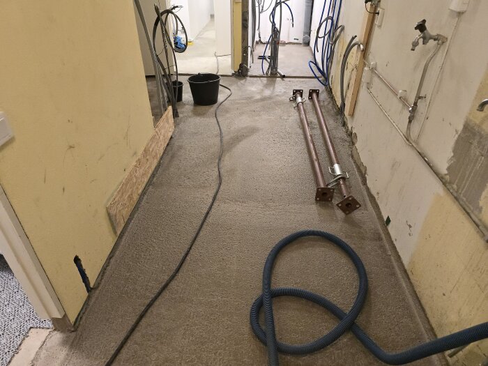 Renoveringsprojekt med ett rum under ombyggnad, synliga rör, vattensystem och kablar, brädor lutande mot väggen.