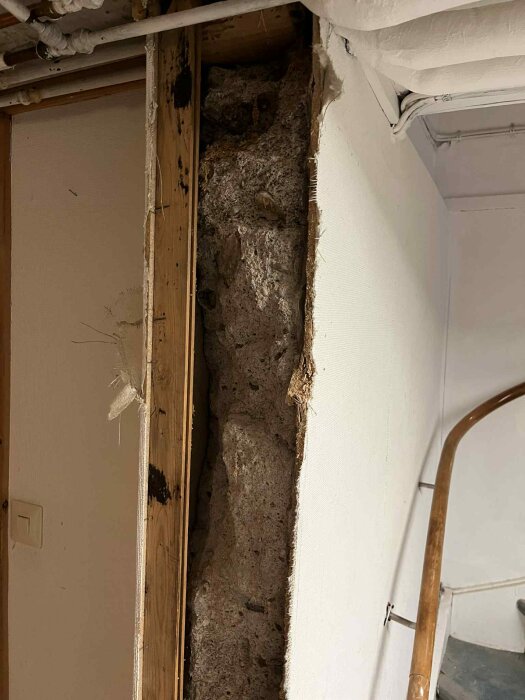 Ojämn bärande vägg med synliga håligheter och löst material i en gammal källare under renovering, omgiven av träreglar och rör.