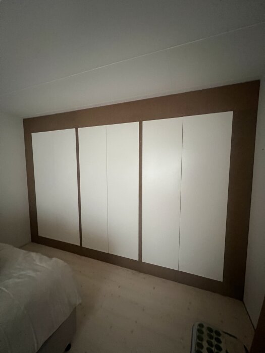 Garderobsvägg med vita dörrar och omgivande MDF-paneler, del av ett projekt för att skapa en inbyggd väggkänsla i sovrum.