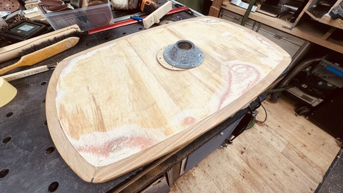 Undersidan av ett teakbord med en monterad fästplatta, placerat på en arbetsbänk, omringad av verktyg och material.