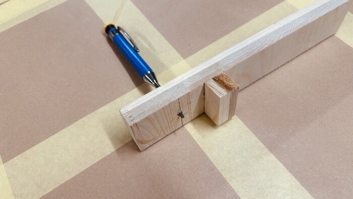 Mätverktyg av trä med penna på brun pappersmall på bordet.