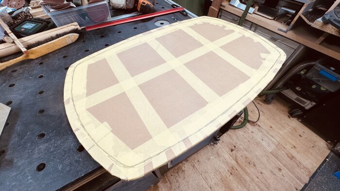 Mall av papper och maskeringstejp på ett teakbord, redo för att forma ett aluminiumblad för att förstärka bordets undersida.