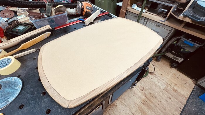 Teakbord med papperstemplate för passning av aluminiumblad i verkstadsmiljö, omgiven av verktyg och material för renovering.