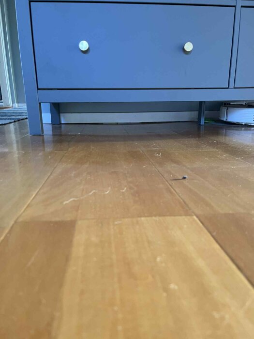 Golv med ojämn yta och en låg blå byrå i bakgrunden, tagen från golvnivå för att visa lutning eller svacka i golvet.