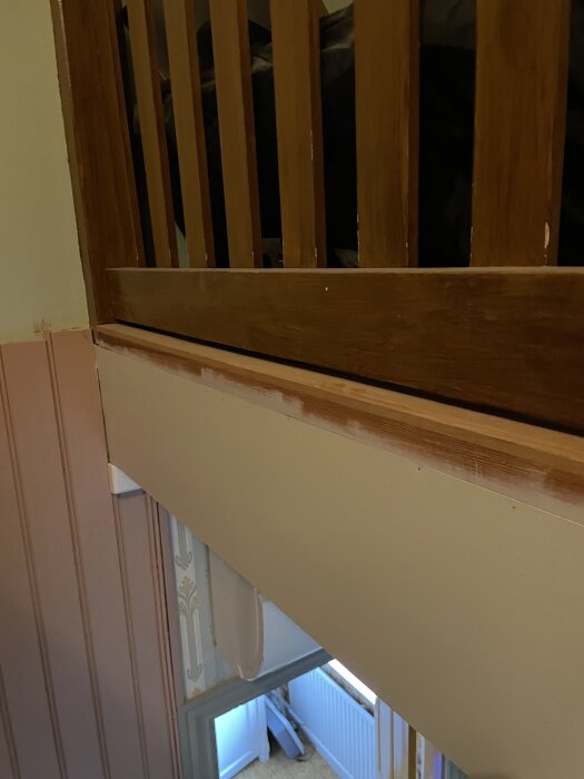 Träräcke över en trappa, del av renovering i övervåning, med ny vägg och färgdetaljer synliga, arbete pågår för att skapa ny ingång över trapphålet.
