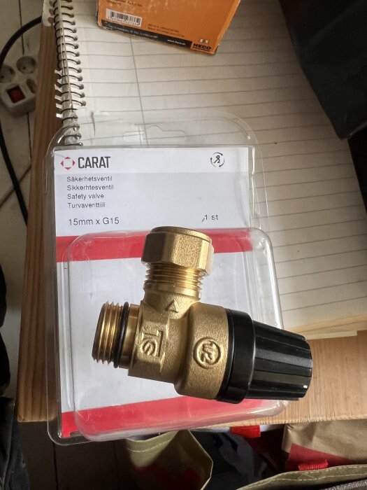 Säkerhetsventil för vattenvärmare i förpackning, märkt Carat, 15mm x G15. Ventilen är i metall med svart plasthandtag.